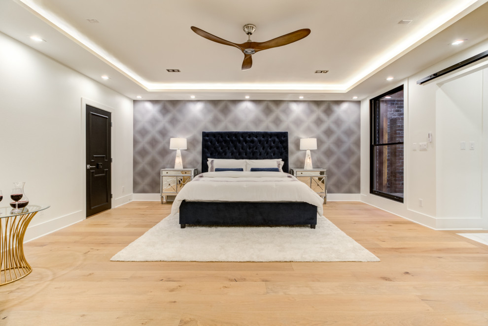 Photo of a large transitional master bedroom in Houston with light hardwood floors, a hanging fireplace, recessed and wallpaper.