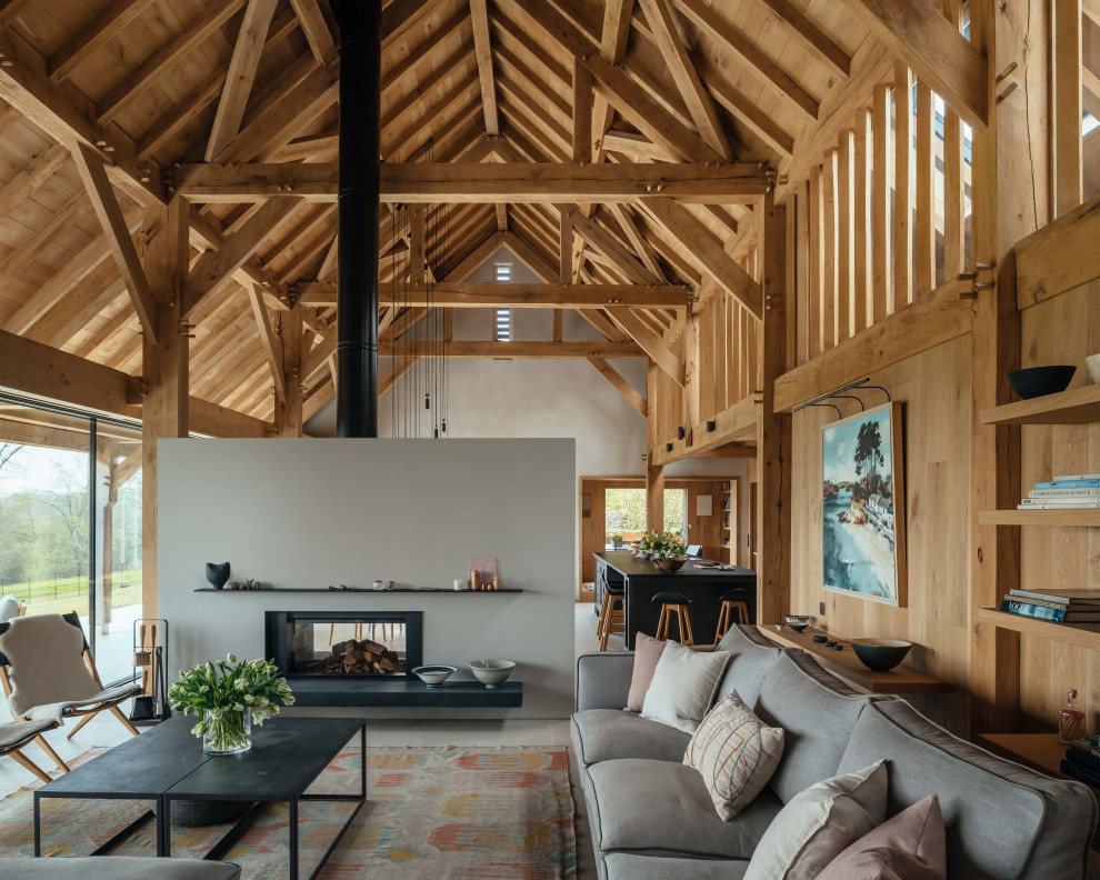 Cette photo montre un salon nature en bois ouvert avec un mur gris, une cheminée double-face, un sol gris, poutres apparentes, un plafond voûté et un plafond en bois.