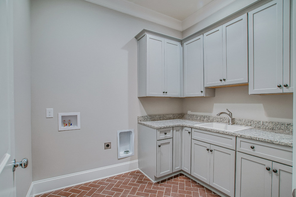 Large traditional l-shaped laundry room in Nashville with a drop-in sink, shaker cabinets, white cabinets, granite benchtops, white walls and terra-cotta floors.
