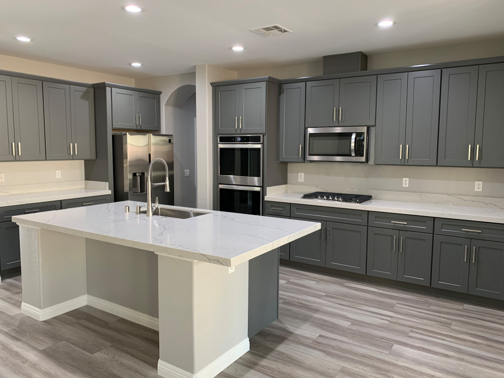 Large contemporary eat-in kitchen in Las Vegas with an undermount sink, shaker cabinets, grey cabinets, quartzite benchtops, stainless steel appliances, laminate floors, with island, grey floor and white benchtop.