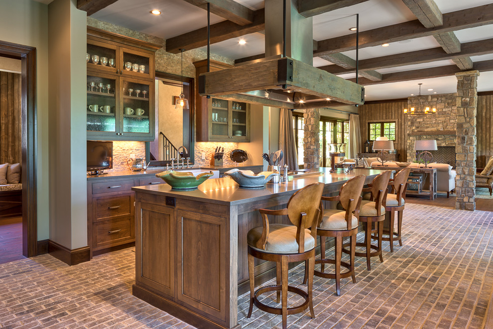 Photo of a large country single-wall open plan kitchen in Other with recessed-panel cabinets, distressed cabinets, quartzite benchtops, beige splashback, mosaic tile splashback, stainless steel appliances, brick floors, with island, beige benchtop and exposed beam.