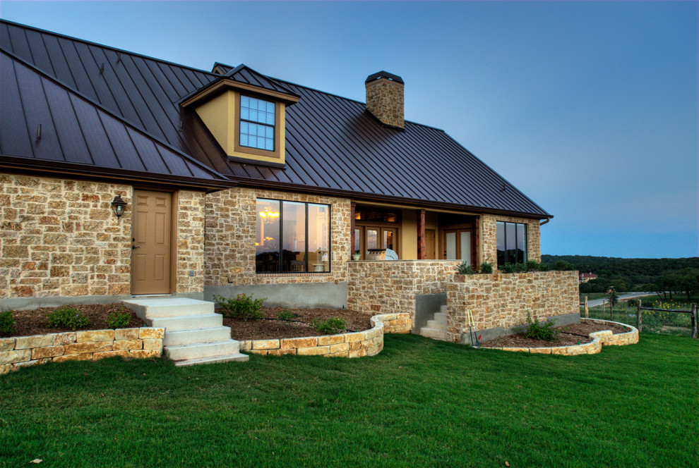 Expansive country two-storey stucco beige house exterior in Austin with a gable roof and a metal roof.