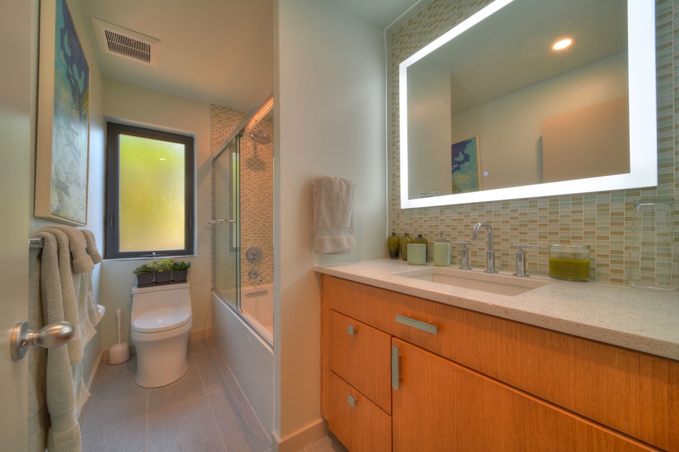 Large midcentury 3/4 bathroom in Miami with flat-panel cabinets, light wood cabinets, porcelain floors, an undermount sink, grey floor, beige tile, blue tile, gray tile, limestone benchtops, beige benchtops, an alcove tub, a shower/bathtub combo, mosaic tile, grey walls and a sliding shower screen.