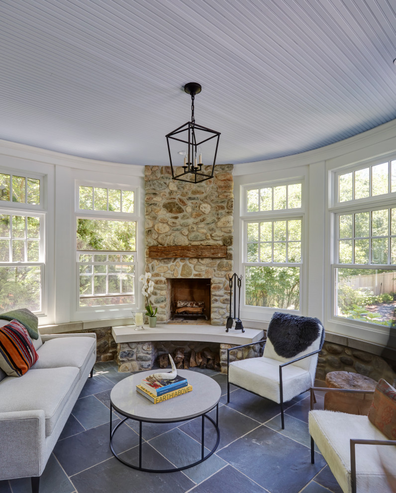 Cette photo montre une grande véranda chic avec un sol en ardoise, une cheminée standard, un manteau de cheminée en pierre, un plafond standard et un sol bleu.