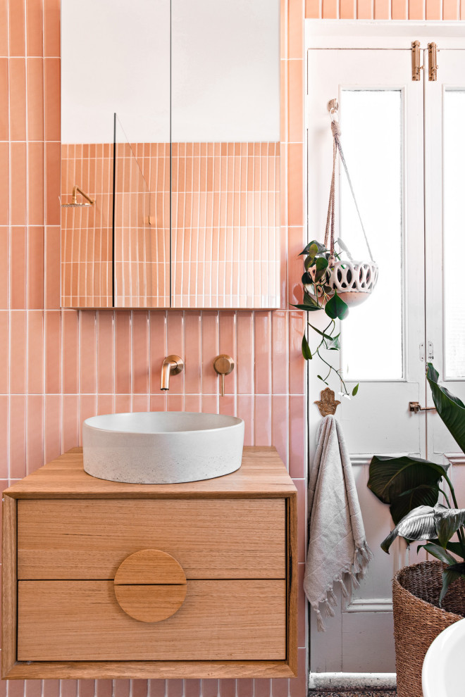 This is an example of a mid-sized scandinavian master bathroom in Sydney with medium wood cabinets, a freestanding tub, an open shower, a two-piece toilet, pink tile, ceramic tile, pink walls, terrazzo floors, a wall-mount sink, wood benchtops, multi-coloured floor, an open shower, brown benchtops, a single vanity and a floating vanity.