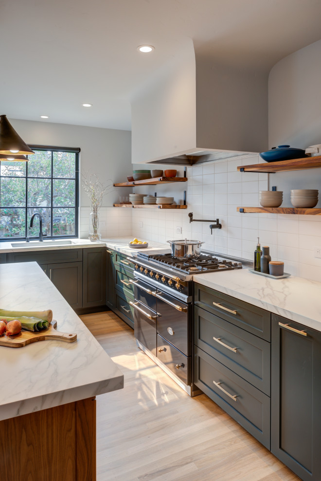 This is an example of a large transitional l-shaped eat-in kitchen in San Francisco with an undermount sink, shaker cabinets, green cabinets, quartz benchtops, white splashback, ceramic splashback, black appliances, light hardwood floors, with island and white benchtop.