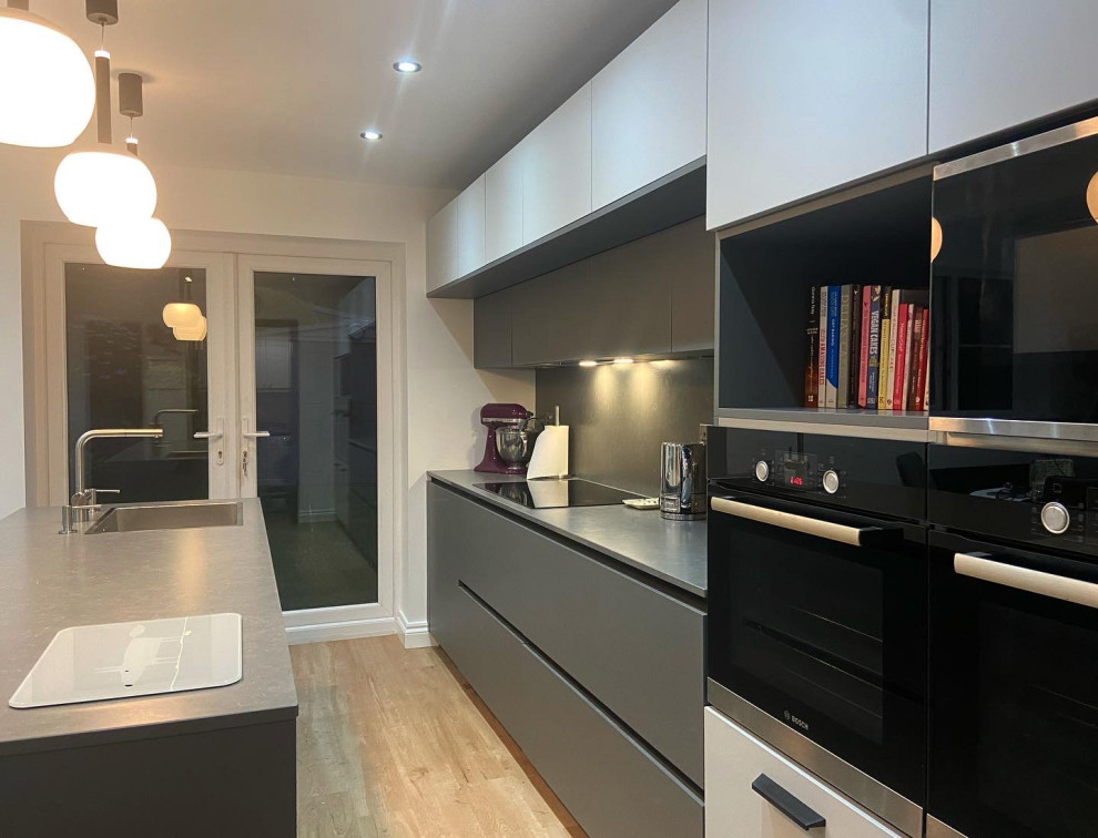 Inspiration for a mid-sized modern l-shaped eat-in kitchen in Manchester with a drop-in sink, flat-panel cabinets, grey cabinets, quartzite benchtops, grey splashback, black appliances, vinyl floors, with island and grey benchtop.