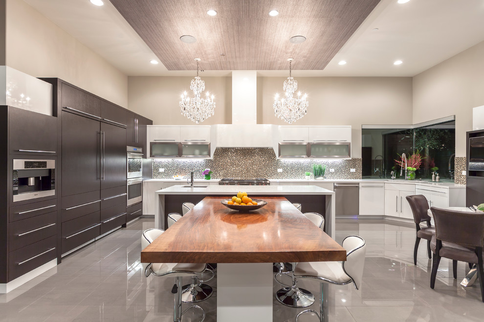 This is an example of a large contemporary u-shaped eat-in kitchen in Las Vegas with flat-panel cabinets, brown cabinets, metallic splashback, mosaic tile splashback, with island, an undermount sink, solid surface benchtops, panelled appliances and porcelain floors.