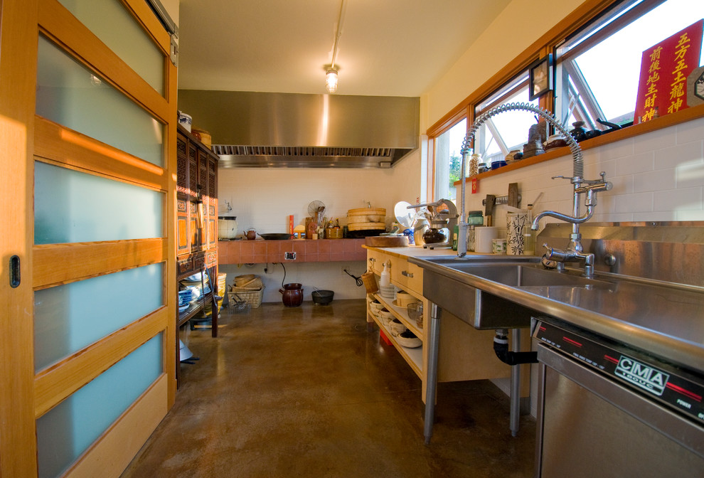 Photo of a mid-sized contemporary l-shaped separate kitchen in Portland with stainless steel appliances, a single-bowl sink, stainless steel benchtops and concrete floors.