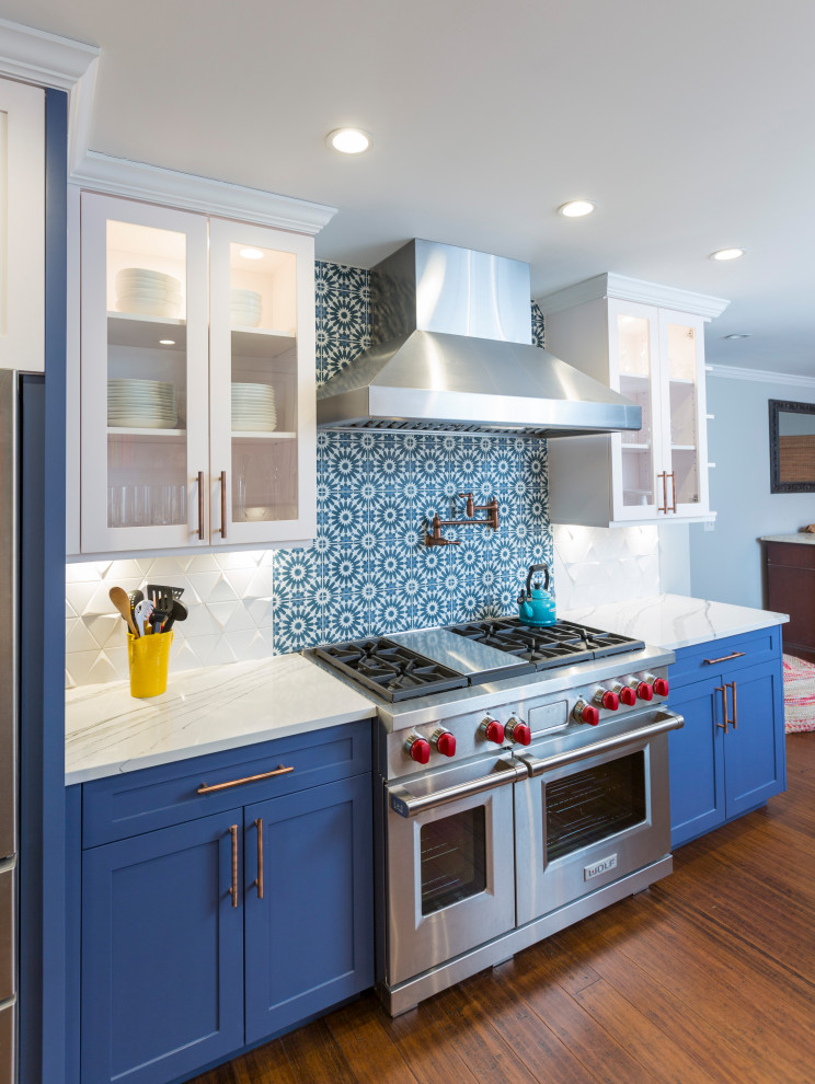 Photo of an eat-in kitchen in Cincinnati with a farmhouse sink, recessed-panel cabinets, blue cabinets, quartz benchtops, white splashback, glass tile splashback, stainless steel appliances, bamboo floors, a peninsula, brown floor and white benchtop.