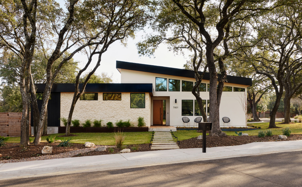 Inspiration for a large midcentury one-storey beige house exterior in Austin with mixed siding, a flat roof, a metal roof, a black roof and board and batten siding.