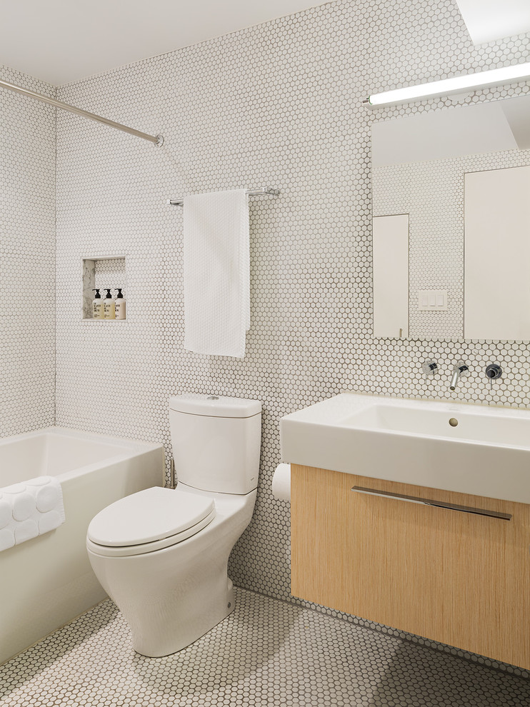 This is an example of a midcentury bathroom in Philadelphia with a console sink, flat-panel cabinets, light wood cabinets, an alcove tub, a shower/bathtub combo, a two-piece toilet, white tile, mosaic tile and mosaic tile floors.