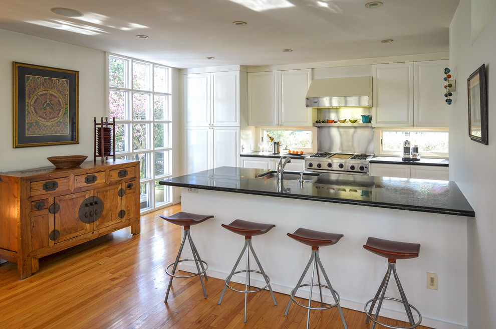 Transitional medium tone wood floor kitchen photo in New York with an undermount sink, white cabinets, stainless steel appliances and a peninsula