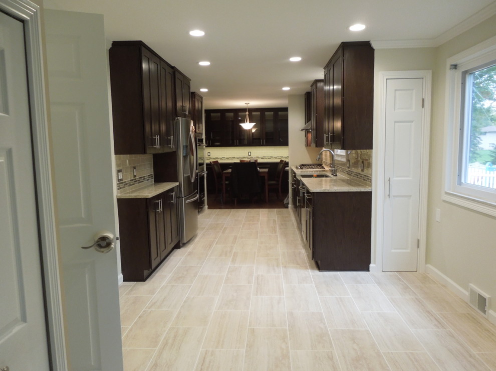 This is an example of a large transitional galley eat-in kitchen in Detroit with a farmhouse sink, shaker cabinets, dark wood cabinets, quartz benchtops, beige splashback, ceramic splashback, stainless steel appliances, ceramic floors, no island and beige floor.