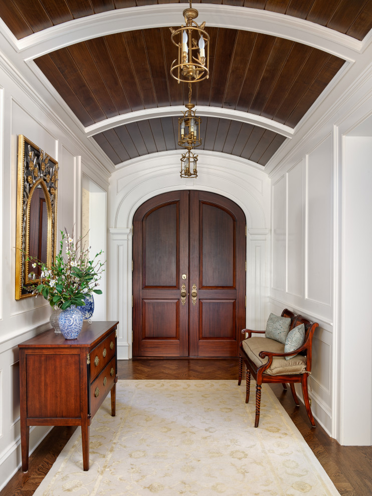Immagine di un grande ingresso tradizionale con pareti marroni, parquet scuro, una porta a due ante, una porta in legno scuro, pavimento marrone, soffitto a volta e boiserie
