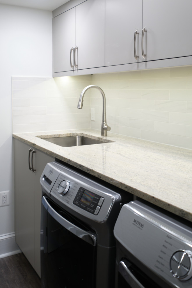 Small contemporary single-wall laundry cupboard in Baltimore with an undermount sink, flat-panel cabinets, grey cabinets, granite benchtops, beige splashback, marble splashback, white walls, a side-by-side washer and dryer and beige benchtop.