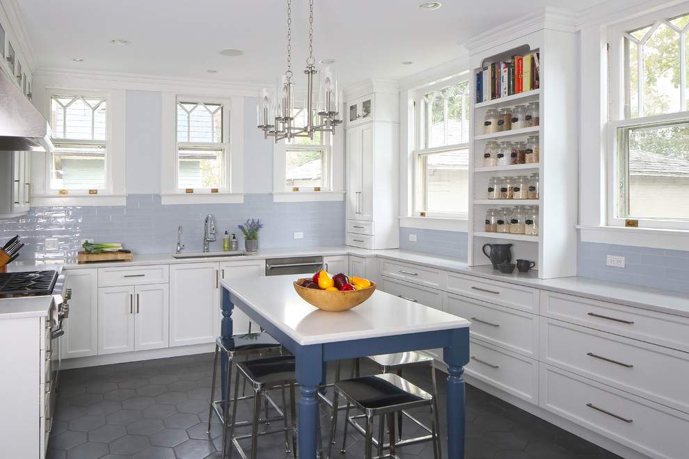 This is an example of a beach style u-shaped kitchen in New York with an undermount sink, shaker cabinets, white cabinets, blue splashback, subway tile splashback, stainless steel appliances, with island, grey benchtop and black floor.