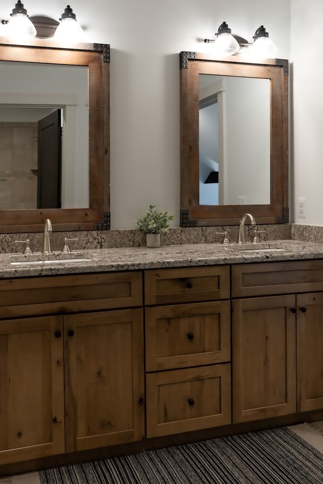 This is an example of a mid-sized country master bathroom in Detroit with shaker cabinets, medium wood cabinets, an alcove shower, a two-piece toilet, brown tile, stone tile, white walls, porcelain floors, granite benchtops, beige floor, a sliding shower screen and brown benchtops.