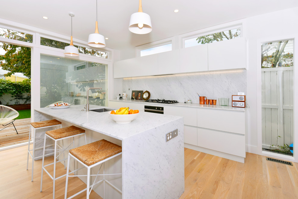 This is an example of a mid-sized traditional galley eat-in kitchen in Auckland with an undermount sink, recessed-panel cabinets, white cabinets, marble benchtops, white splashback, subway tile splashback, stainless steel appliances, light hardwood floors and with island.