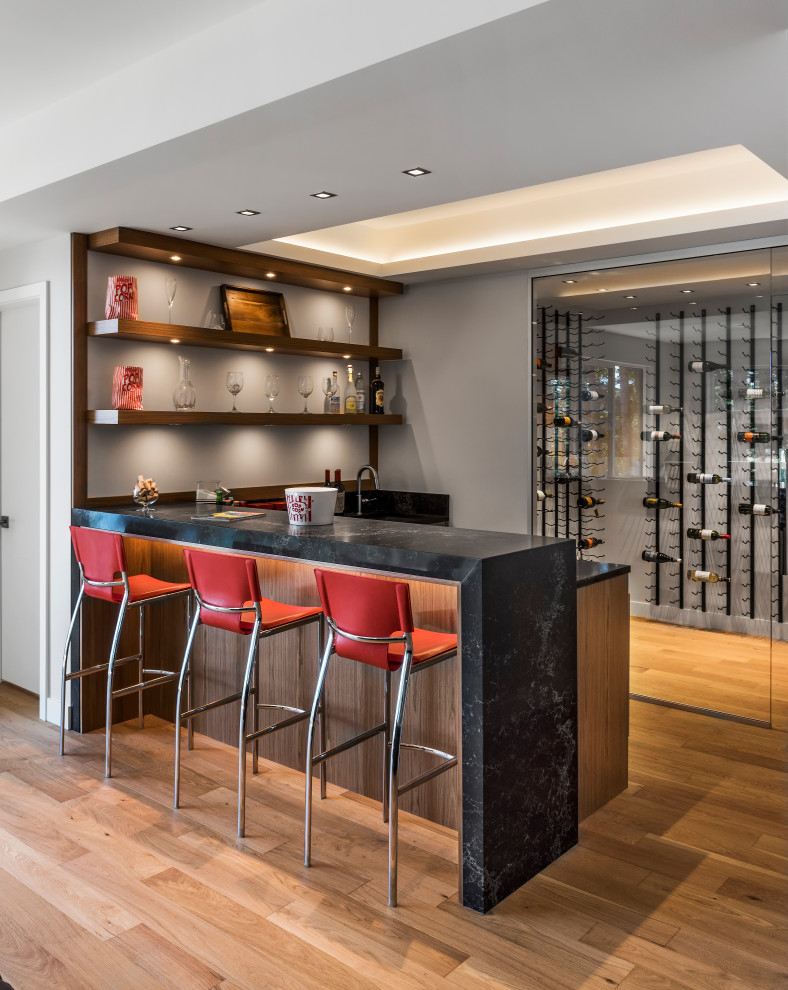 Design ideas for a large contemporary l-shaped seated home bar in Other with quartz benchtops, light hardwood floors and black benchtop.