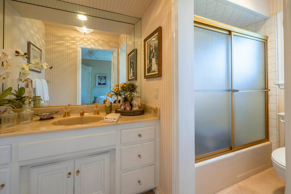 Inspiration for a mid-sized traditional master bathroom in Los Angeles with raised-panel cabinets, white cabinets, an alcove tub, a shower/bathtub combo, a two-piece toilet, white tile, porcelain tile, beige walls, ceramic floors, an integrated sink, marble benchtops, beige floor and a sliding shower screen.