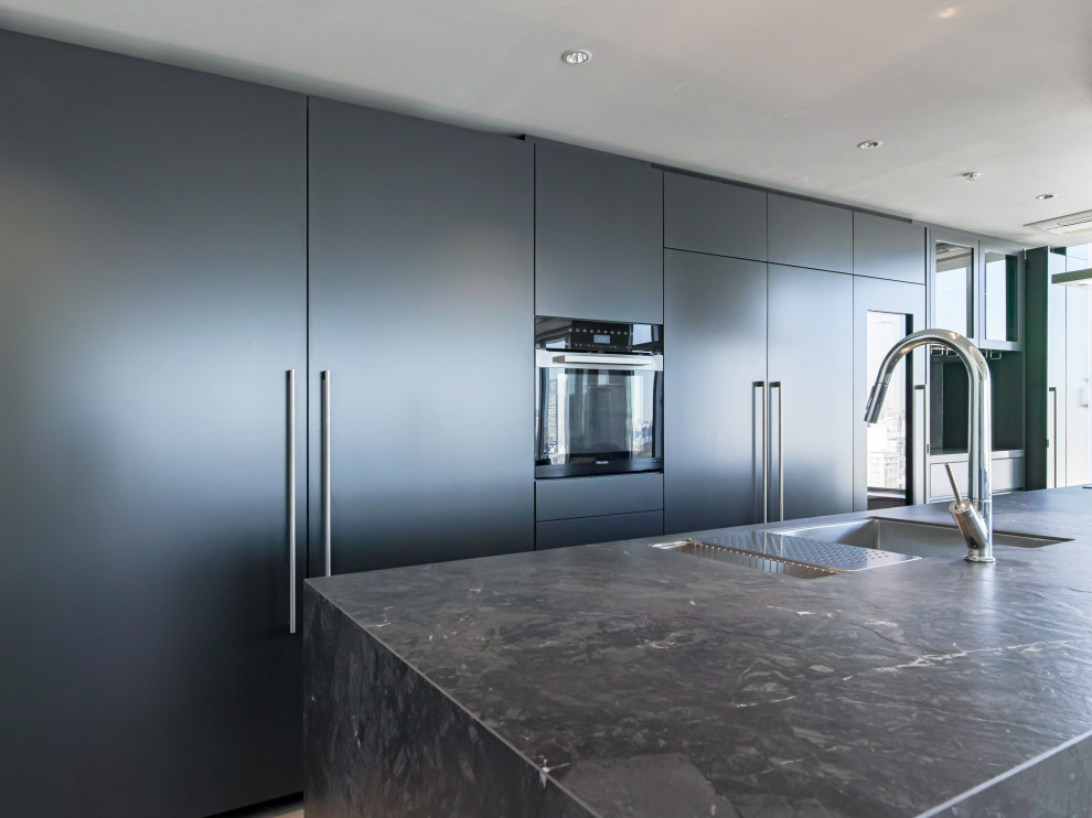 Aménagement d'une cuisine ouverte parallèle moderne avec des portes de placard grises, plan de travail carrelé, îlot et plan de travail noir.