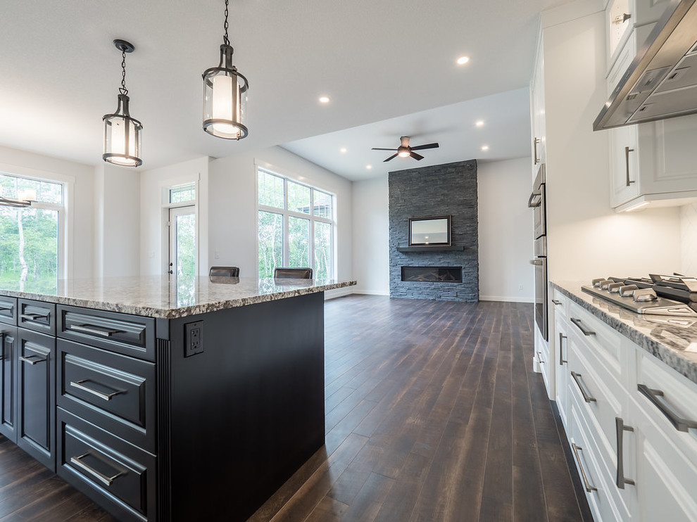 This is an example of a mid-sized contemporary l-shaped eat-in kitchen in Edmonton with a double-bowl sink, raised-panel cabinets, white cabinets, quartzite benchtops, white splashback, porcelain splashback, stainless steel appliances, laminate floors, with island and brown floor.