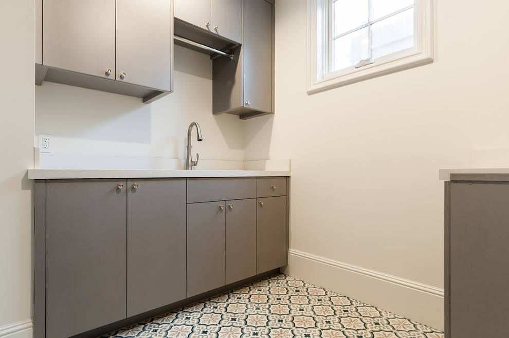 This is an example of a mid-sized country u-shaped dedicated laundry room in Los Angeles with an undermount sink, flat-panel cabinets, grey cabinets, solid surface benchtops, white walls, ceramic floors, a side-by-side washer and dryer, blue floor and white benchtop.