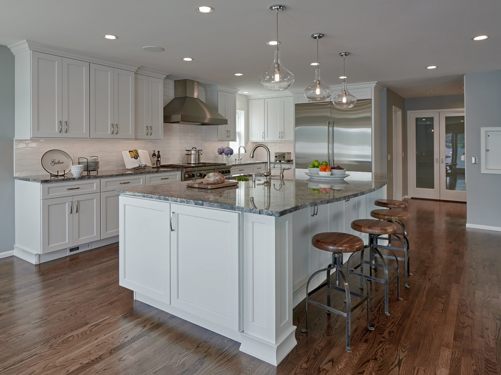 Design ideas for a large arts and crafts single-wall eat-in kitchen in Seattle with a drop-in sink, shaker cabinets, white cabinets, white splashback, ceramic splashback, stainless steel appliances, dark hardwood floors, with island, granite benchtops, brown floor and grey benchtop.