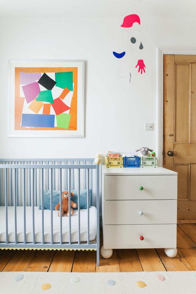 This is an example of a bohemian nursery in Sussex with white walls, medium hardwood flooring and brown floors.