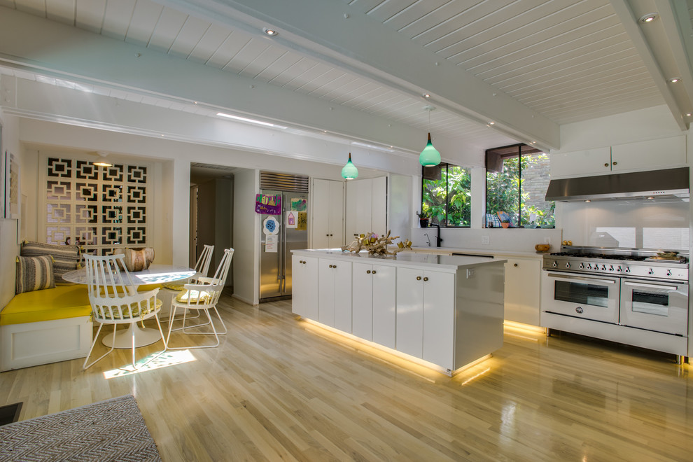 Inspiration for an eclectic kitchen in Dallas with a drop-in sink, flat-panel cabinets, white cabinets, quartz benchtops, white splashback, glass sheet splashback, white appliances, light hardwood floors and with island.