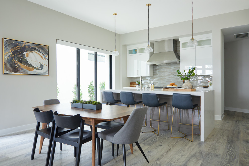 Photo of a mid-sized contemporary galley eat-in kitchen in Los Angeles with flat-panel cabinets, white cabinets, glass tile splashback, medium hardwood floors, with island, grey floor, white benchtop and beige splashback.