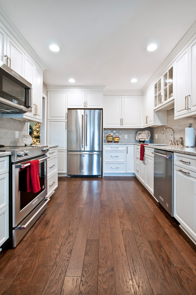 This is an example of a small transitional l-shaped separate kitchen in Nashville with an undermount sink, raised-panel cabinets, white cabinets, quartz benchtops, grey splashback, ceramic splashback, stainless steel appliances, medium hardwood floors, no island, brown floor and white benchtop.