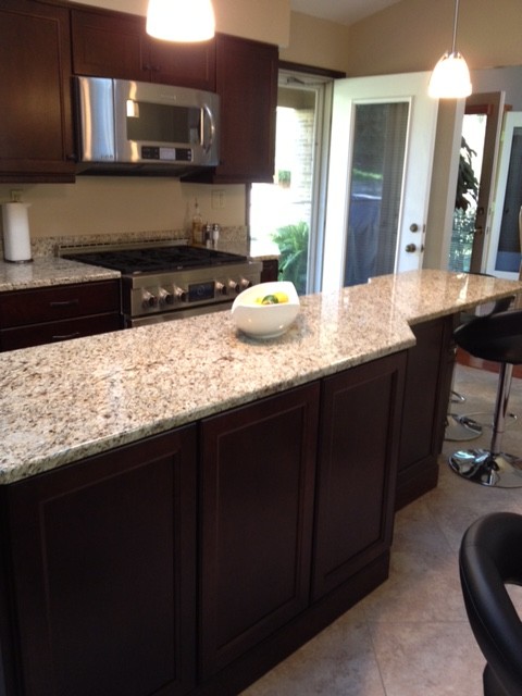 Inspiration for a transitional porcelain tile eat-in kitchen remodel with a double-bowl sink, recessed-panel cabinets, brown cabinets, granite countertops, beige backsplash, stone slab backsplash, stainless steel appliances and an island