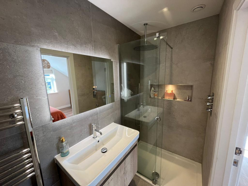 Modern inredning av ett litet badrum, med släta luckor, skåp i ljust trä, en öppen dusch, en vägghängd toalettstol, grå kakel, keramikplattor, beige väggar, klinkergolv i keramik, ett väggmonterat handfat, beiget golv och dusch med skjutdörr