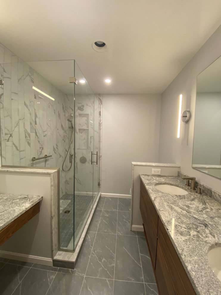 Small contemporary master bathroom in Baltimore with flat-panel cabinets, medium wood cabinets, a corner shower, a one-piece toilet, gray tile, porcelain tile, grey walls, porcelain floors, an undermount sink, granite benchtops, grey floor, a hinged shower door, grey benchtops, a shower seat, a double vanity and a built-in vanity.