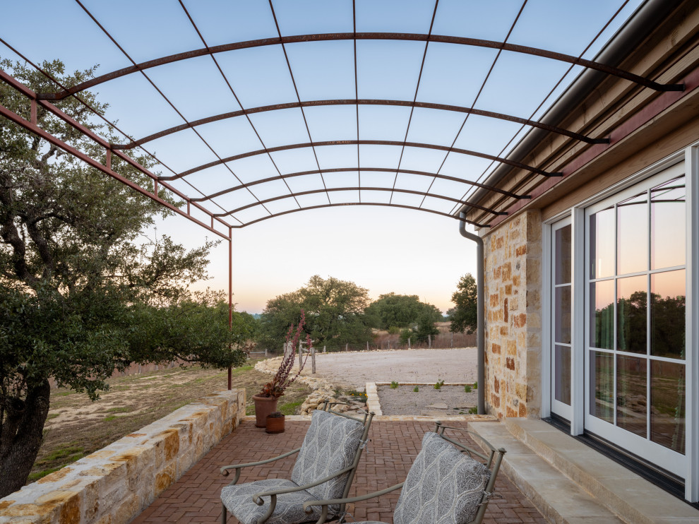 Country brick patio photo in Austin with a pergola
