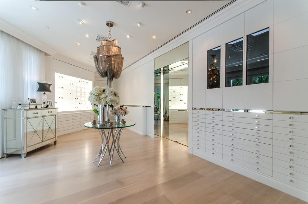 Expansive contemporary women's dressing room in Miami with flat-panel cabinets, white cabinets and light hardwood floors.