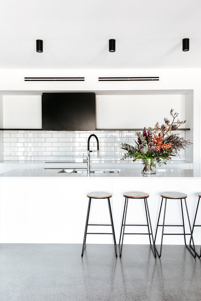 Mid-sized contemporary galley kitchen in Wollongong with a double-bowl sink, flat-panel cabinets, white cabinets, quartz benchtops, white splashback, ceramic splashback, concrete floors, with island, grey floor and white benchtop.