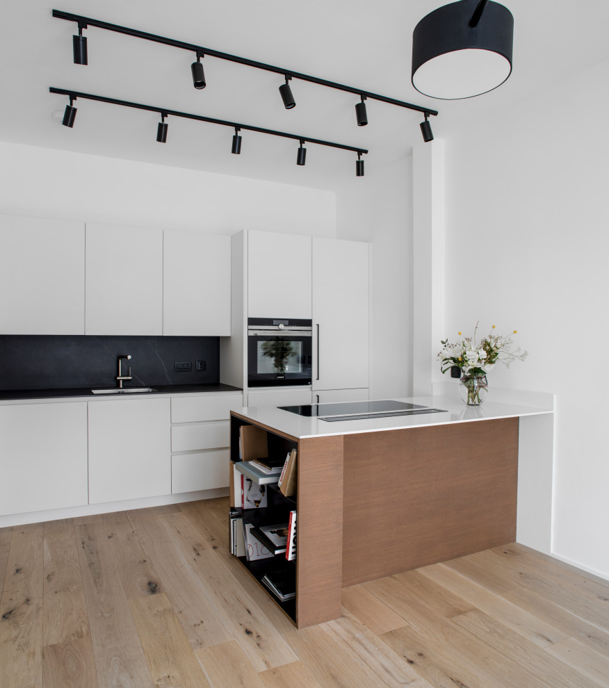This is an example of a mid-sized contemporary galley kitchen in London with flat-panel cabinets, white cabinets, black splashback, panelled appliances, light hardwood floors, a peninsula, beige floor and white benchtop.
