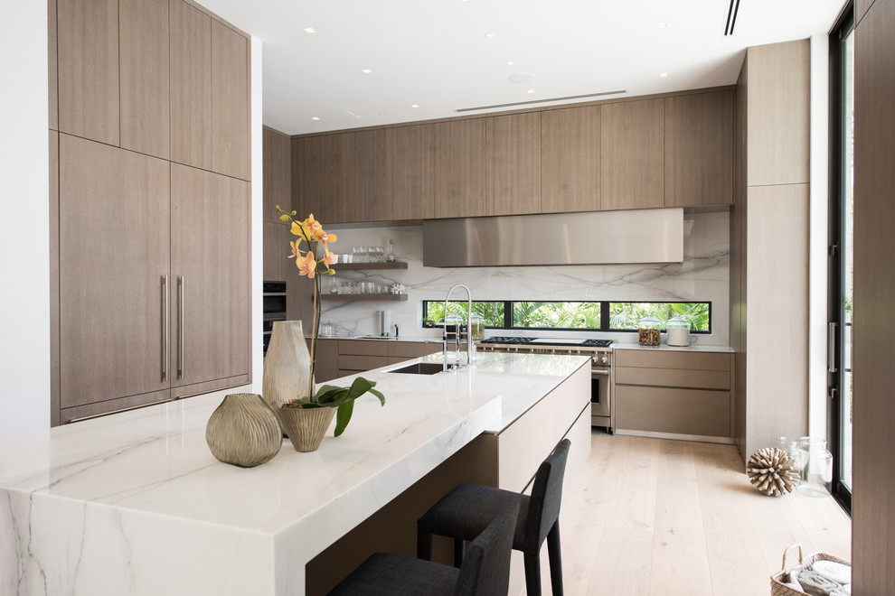 Inspiration for a contemporary kitchen in Miami with an undermount sink, flat-panel cabinets, white splashback, stainless steel appliances, light hardwood floors, with island and light wood cabinets.