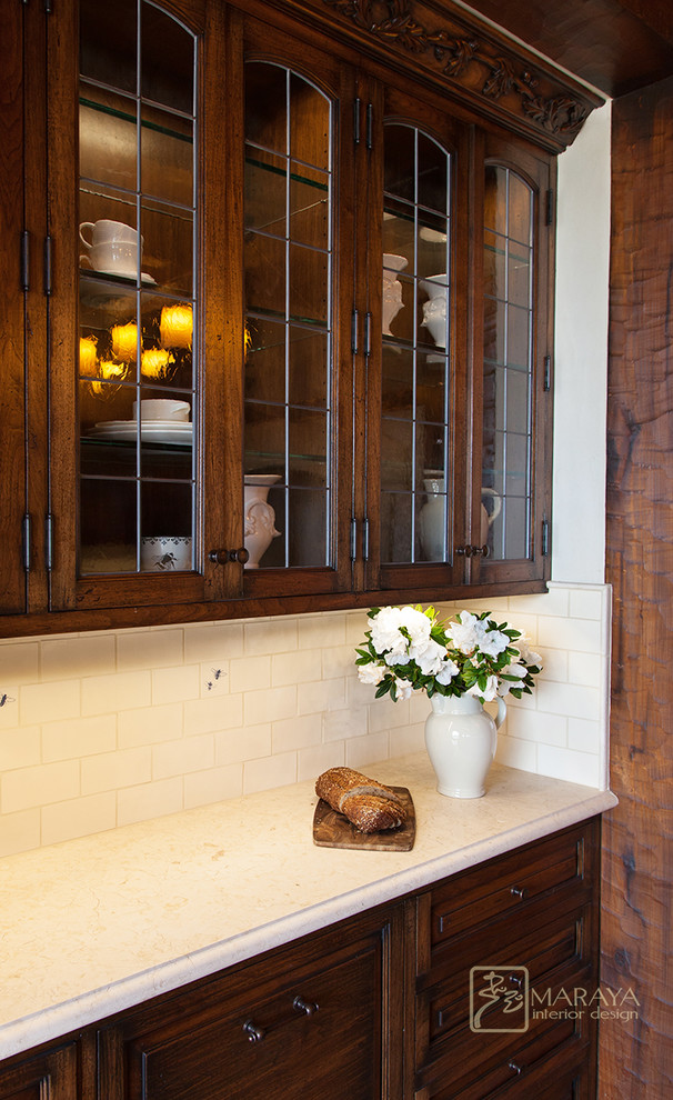 Photo of a mid-sized country u-shaped kitchen in Santa Barbara with a farmhouse sink, raised-panel cabinets, distressed cabinets, marble benchtops, white splashback, ceramic splashback, panelled appliances and limestone floors.