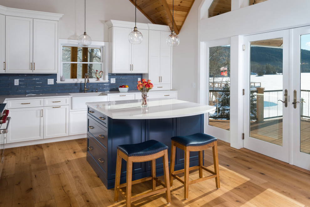 Design ideas for a mid-sized transitional l-shaped eat-in kitchen in Burlington with a farmhouse sink, shaker cabinets, white cabinets, quartz benchtops, blue splashback, ceramic splashback, with island and white benchtop.