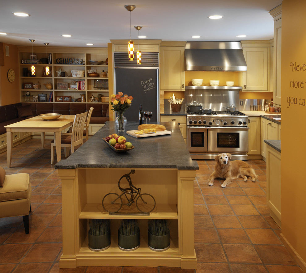 Photo of a mid-sized mediterranean eat-in kitchen in Detroit with yellow cabinets, soapstone benchtops, shaker cabinets, panelled appliances, terra-cotta floors and with island.