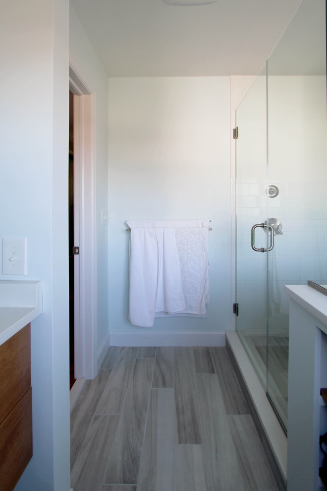 Inspiration for a mid-sized modern master bathroom in Philadelphia with flat-panel cabinets, medium wood cabinets, a corner shower, a two-piece toilet, multi-coloured tile, white walls, terra-cotta floors, an undermount sink, grey floor, a hinged shower door, white benchtops, engineered quartz benchtops and glass tile.