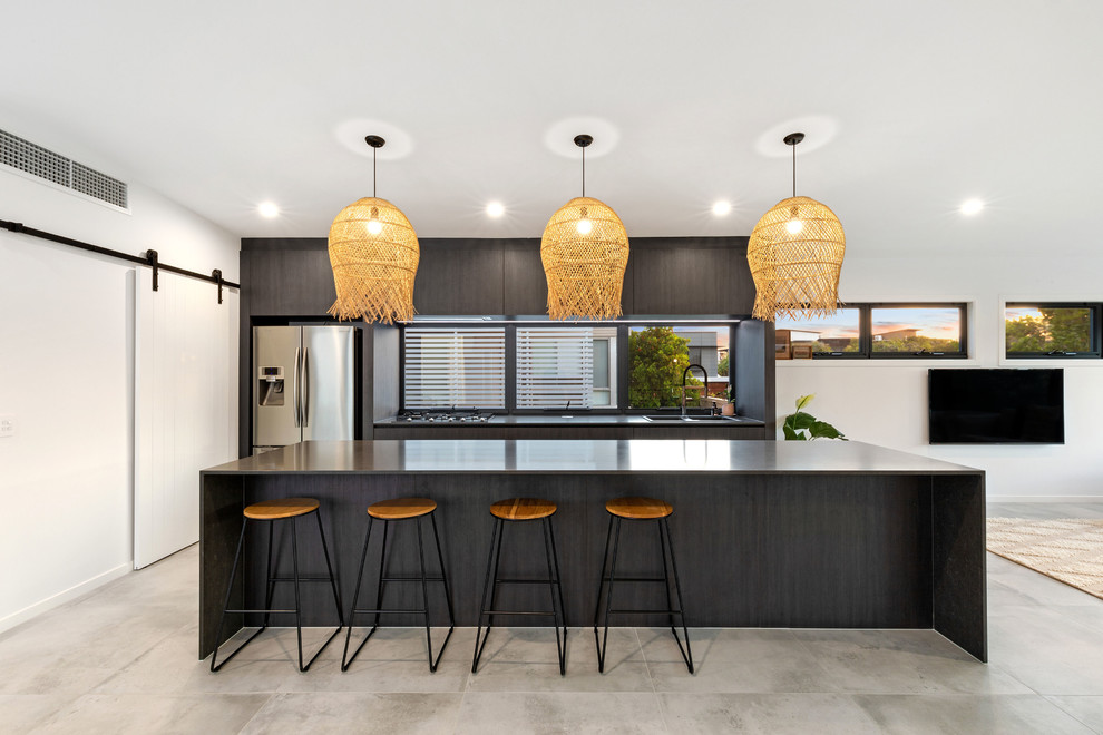 Photo of a beach style single-wall open plan kitchen in Sunshine Coast with a drop-in sink, flat-panel cabinets, black cabinets, granite benchtops, glass sheet splashback, porcelain floors, with island, grey floor, black benchtop and stainless steel appliances.