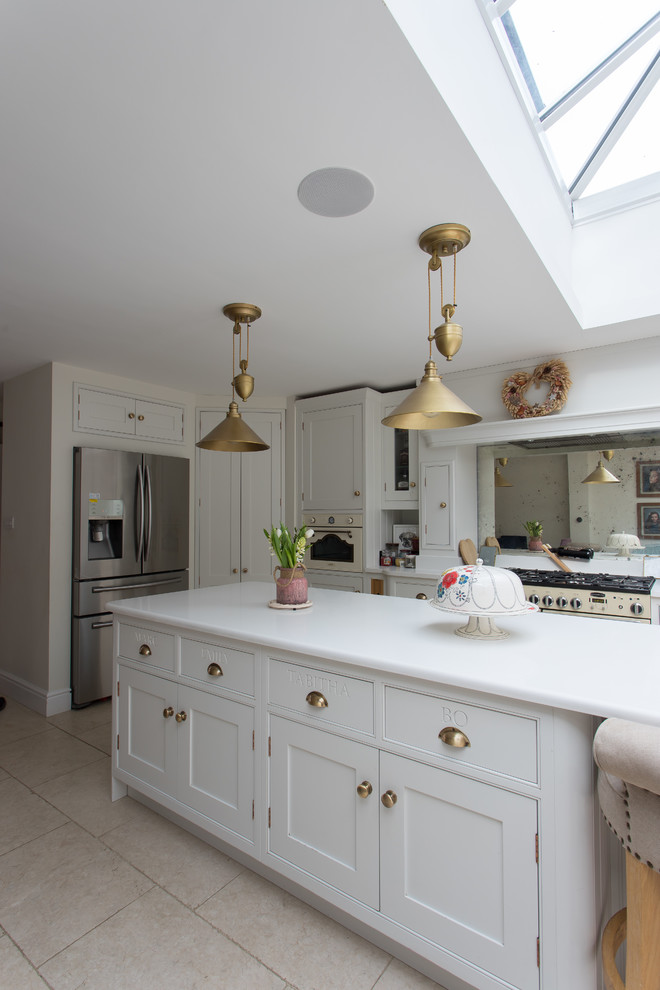 Photo of a large traditional l-shaped eat-in kitchen in Hertfordshire with a single-bowl sink, shaker cabinets, yellow cabinets, soapstone benchtops, metallic splashback, mirror splashback, stainless steel appliances, porcelain floors, with island, beige floor and white benchtop.