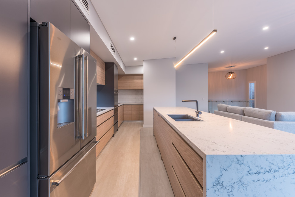 Inspiration for a contemporary galley open plan kitchen in Perth with an undermount sink, flat-panel cabinets, medium wood cabinets, quartz benchtops, white splashback, subway tile splashback, stainless steel appliances, light hardwood floors, with island and beige floor.