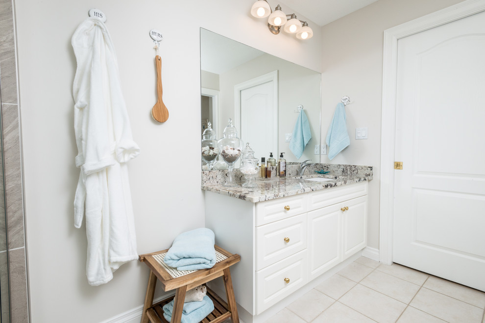 Inspiration for a small transitional master bathroom in Edmonton with shaker cabinets, white cabinets, a corner tub, a corner shower, a one-piece toilet, multi-coloured tile, pebble tile, beige walls, porcelain floors, a drop-in sink and granite benchtops.