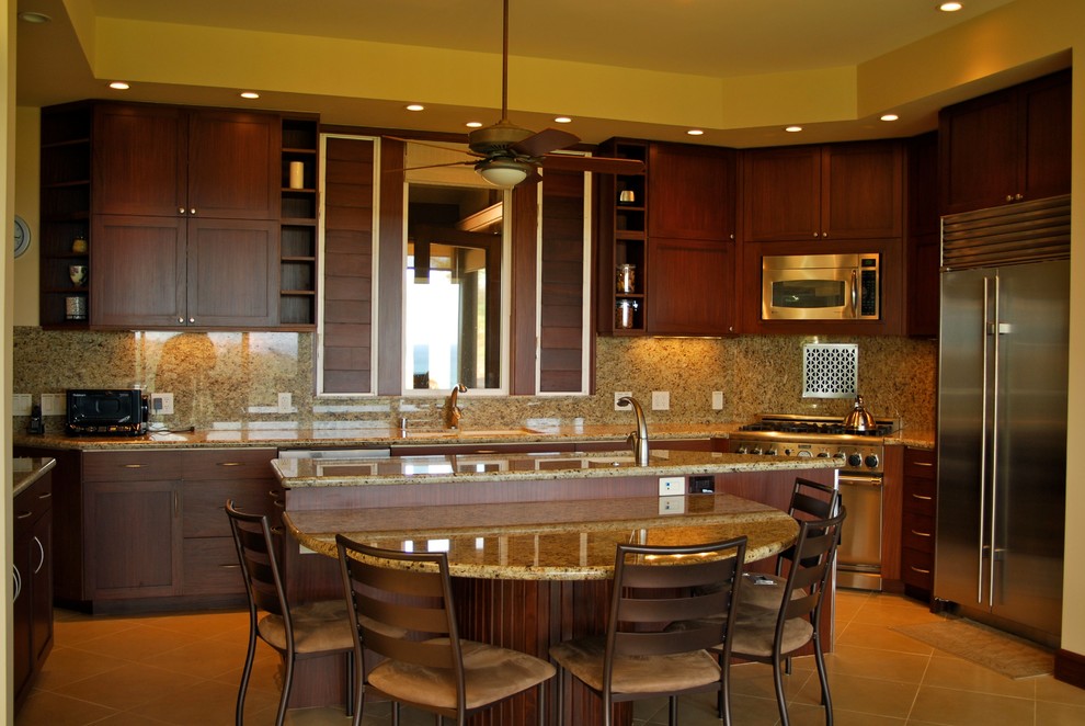 This is an example of a mid-sized tropical u-shaped eat-in kitchen in Hawaii with an undermount sink, shaker cabinets, dark wood cabinets, granite benchtops, stone slab splashback, stainless steel appliances, ceramic floors, with island, brown floor, beige splashback and beige benchtop.